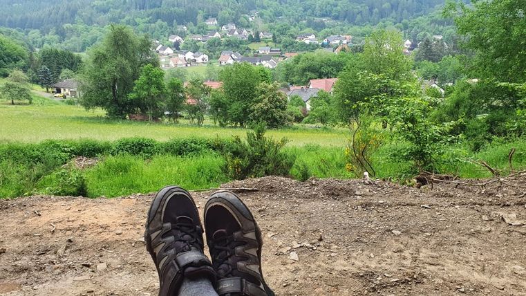 Blick auf den Ort Müsch im Vordergrund sind Wanderschuhe zu sehen