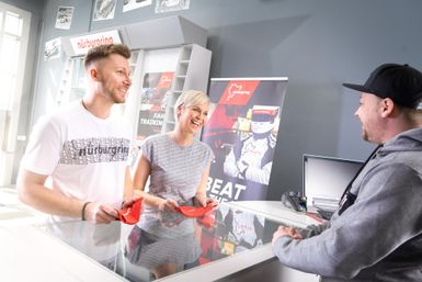 Ein freundliches Gespräch an einem Empfangstresen. Ein Paar, das rot-weiße Schlüssel in der Hand hält, wird von einem Mitarbeiter beraten.