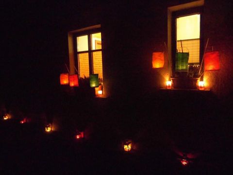 Ein dunkles Fenster mit bunten Laternen und warmem Licht. Die Stimmung ist einladend und festlich.
