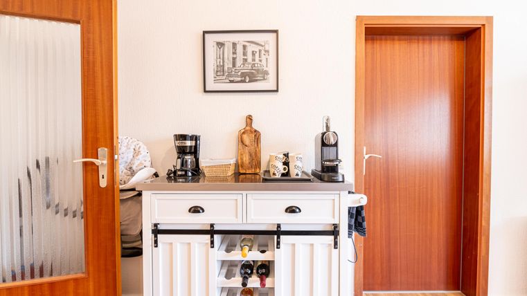 Een lichte kamer met een witte bar en een koffiezetapparaat. Op de achtergrond zijn twee deuren en een ingelijst schilderij te zien.