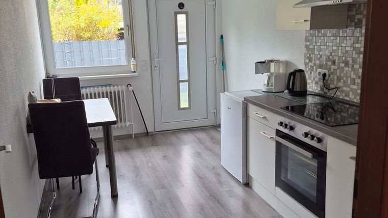 A modern kitchen with a stove, a sink, and a refrigerator-freezer combination. There is a table with chairs and a large window that lets in daylight.