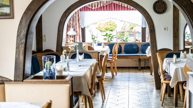 Ein gemütliches Restaurant mit Holzarchitektur und gedeckten Tischen. Im Hintergrund sieht man eine einladende Sitzecke mit Blick ins Freie.