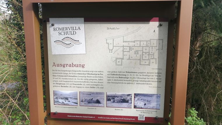 Ein Informationsschild über die Ausgrabung der Romervilla in Schuld. Es zeigt eine Karte und Bilder, die die archäologischen Funde darstellen.