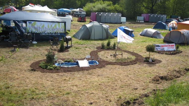 Un campement avec plusieurs tentes et un petit jardin. Des bannières colorées et des plantes décorent les alentours.