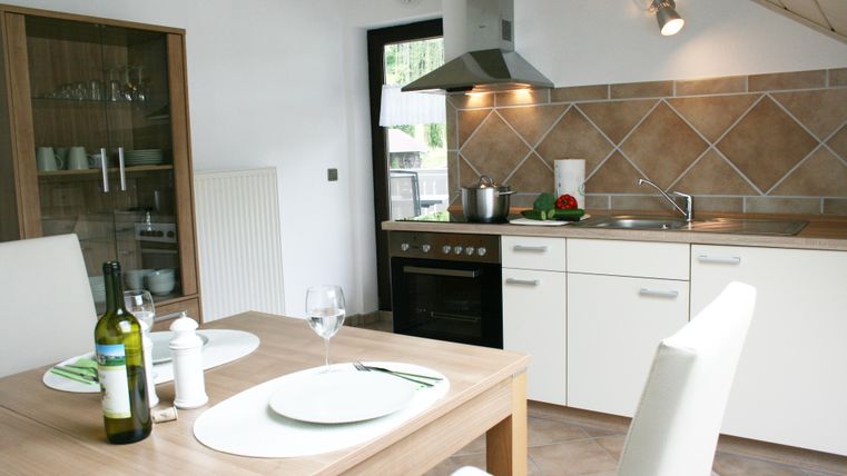 Eine moderne Küche mit Edelstahlgeräten und einem Esstisch. Auf dem Tisch stehen Weinflaschen und Glaswaren.