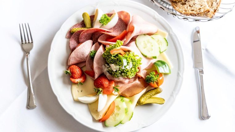 Een bord met verschillende soorten vleeswaren, groenten en fruit. Naast ligt een mand met brood.