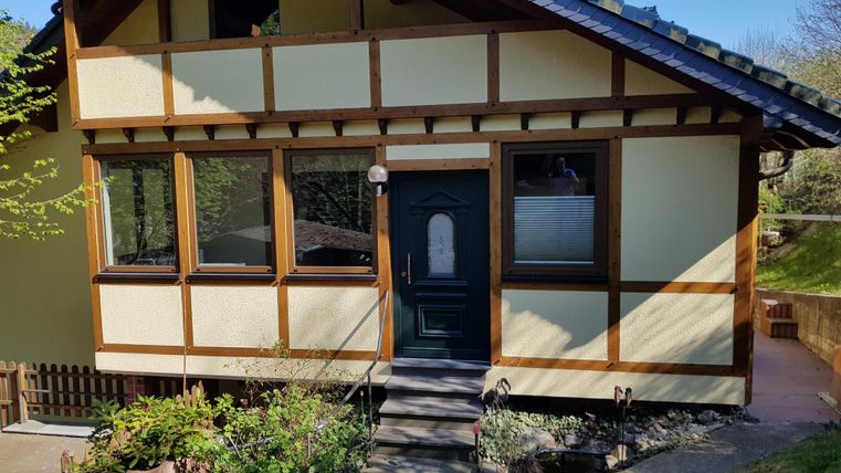 Une maison charmante à colombages avec une entrée verte. Le jardin a des fleurs et est bien entretenu.