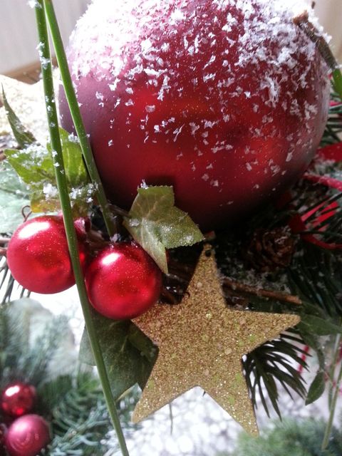 Eine rote Weihnachtskugel mit Schnee, umgeben von grünen Blättern und goldenen Sternen. Dekorative rote Beeren ergänzen die festliche Stimmung.