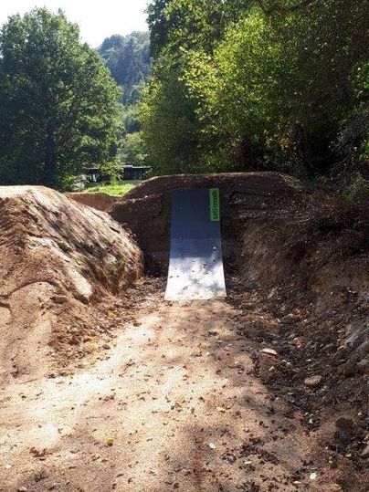 Eine Rampe in einem Waldgebiet, umgeben von Bäumen und Erde. Der Boden ist uneben und die Sonne scheint durch die Blätter.