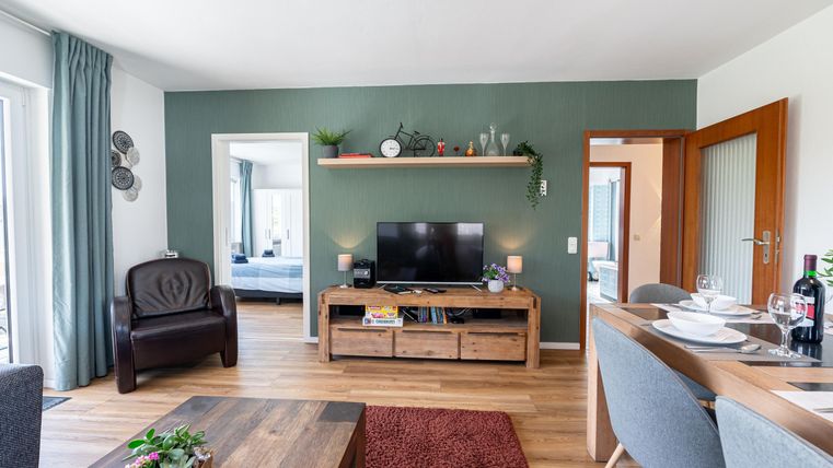 Een moderne woonkamer met een televisie en een gezellige zithoek. De muren zijn geschilderd in een rustgevende groene kleur en de vloer is van hout.