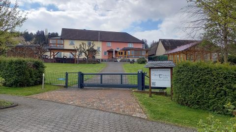 Ein Haus mit mehreren Etagen und einem schönen Garten. Der Eingang zeigt eine Einfahrt mit einem Tor und einem Weg zur Haustür.