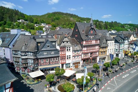 Eine malerische Stadt mit gut erhaltenen Fachwerkhäusern und grünen Hügeln im Hintergrund. Die Straßen sind einladend mit Cafés und Bäumen gesäumt.