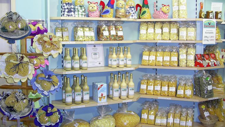 Ein bunt dekorierter Laden mit Regalen voller Pasta, Säfte und kleinen Geschenkartikeln. Oben befinden sich auch dekorative Figuren aus Stoff.