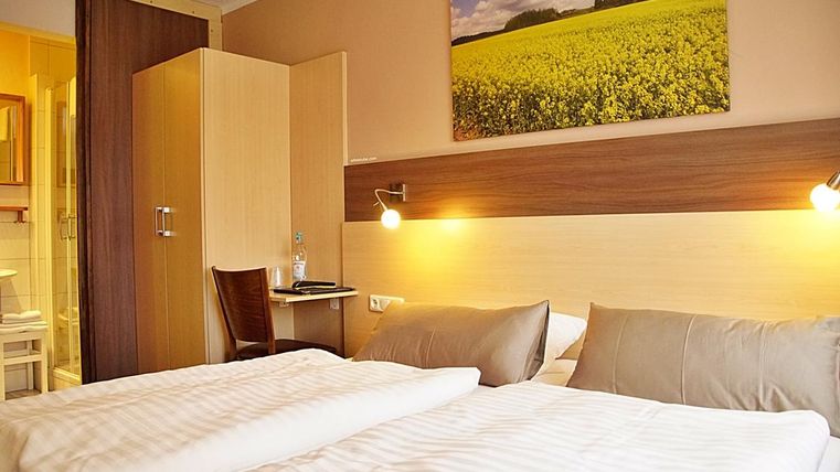 Une chambre d'hôtel confortable avec deux lits et un éclairage doux. En arrière-plan, on peut voir une image d'un beau paysage avec un champ jaune.