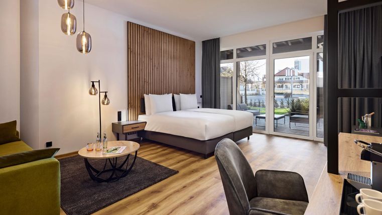 Een moderne kamer met een groot bed, een groene bank en grote ramen. De kamer is helder en stijlvol ingericht, met uitzicht op de buitenruimte.