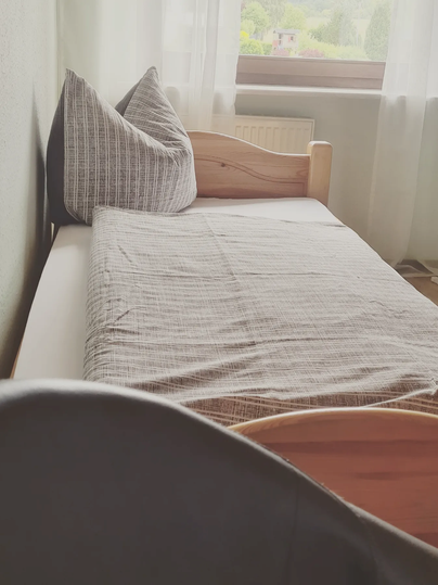 A simple bed with striped pillows in a bright room. The window lets in plenty of daylight.
