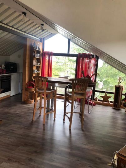 A cozy living kitchen with wooden tables and chairs. Large windows let in plenty of daylight and offer a view of the greenery.