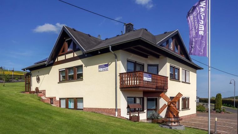 Ein schönes Gebäude mit einem modernen Design und einer kleinen Holzterrasse. Im Vordergrund steht eine Fahne, die Willkommen sagt.