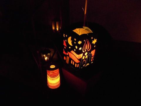 Eine bunte Laterne mit festlichen Motiven leuchtet sanft im Dunkeln. Daneben steht eine kleinere, farbige Laterne, die ebenfalls ein warmes Licht ausstrahlt.