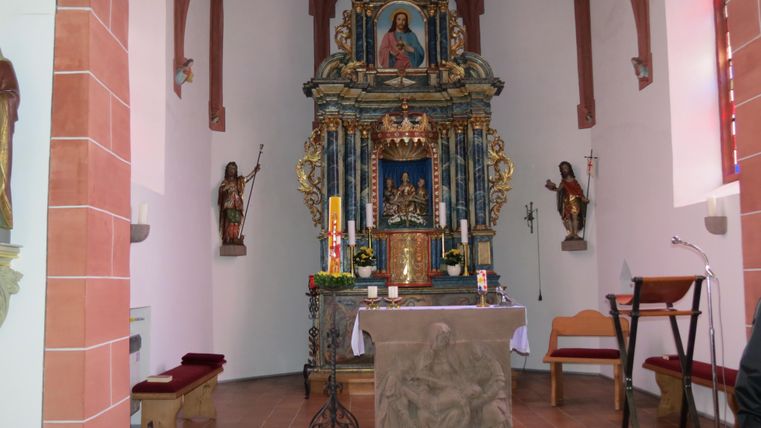 Ein schöner Kircheninnenraum mit einem kunstvoll gestalteten Altar. Die Wände sind geschmückt und es gibt Holzstatuen neben dem Altar.