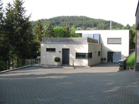 Ein modernes Haus mit einer modernen Architektur in einer ruhigen Umgebung. Im Hintergrund sind Bäume und ein leichter Hügel sichtbar.