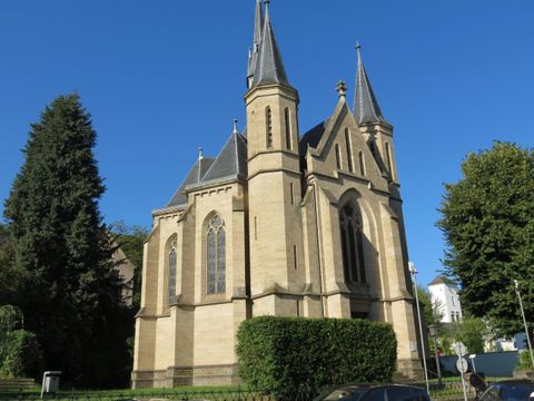 Eine beeindruckende Kirche mit hohen Türmen und großen Fenstern. Sie steht von üppigem Grün umgeben unter einem klaren blauen Himmel.