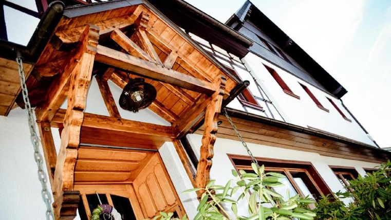 Ein traditionelles Haus mit einem Holzvorbau. Die Fassade ist weiß, und es gibt grüne Pflanzen im Vordergrund.