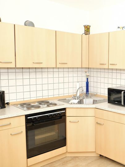 Une cuisine moderne avec des armoires en bois clair et un dosseret en carrelage blanc. Elle est équipée d'une cuisinière, d'un four et d'un micro-ondes.