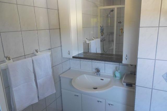 Une salle de bain moderne avec des carreaux blancs et un lavabo. Il y a des serviettes et une douche dans la zone arrière.