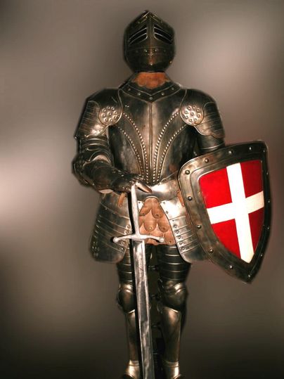 Eine Rüstung eines Ritters steht aufrecht, gehalten mit einem Schild und einem Schwert. Der Ritter trägt eine metallische Rüstung und ist vor einem neutralen Hintergrund platziert.