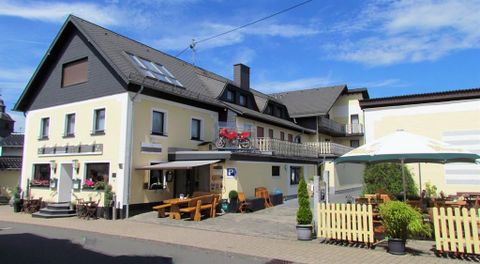 Ein einladendes Gasthaus mit einem großen Außenbereich. Es sind Tische und Stühle auf der Terrasse sowie Sonnenschirme zu sehen.