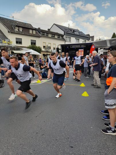 Eine Gruppe von Männern startet ein Rennen auf einer belebten Straße. Um sie herum stehen Zuschauer und Marktstände.
