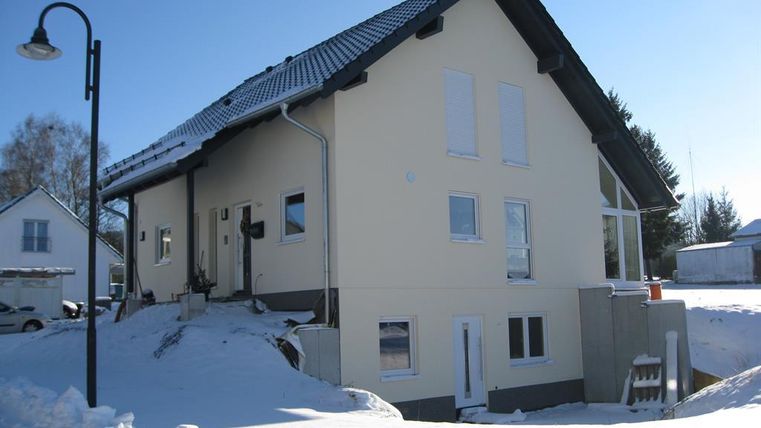 Une maison moderne de deux étages de couleur jaune clair, entourée de neige. Le ciel est clair et bleu.