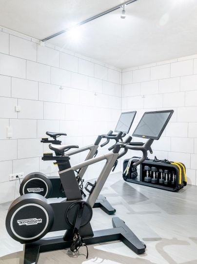 Een moderne fitnessruimte met twee hometrainers en een set gewichten. De wanden zijn licht en eenvoudig gehouden.