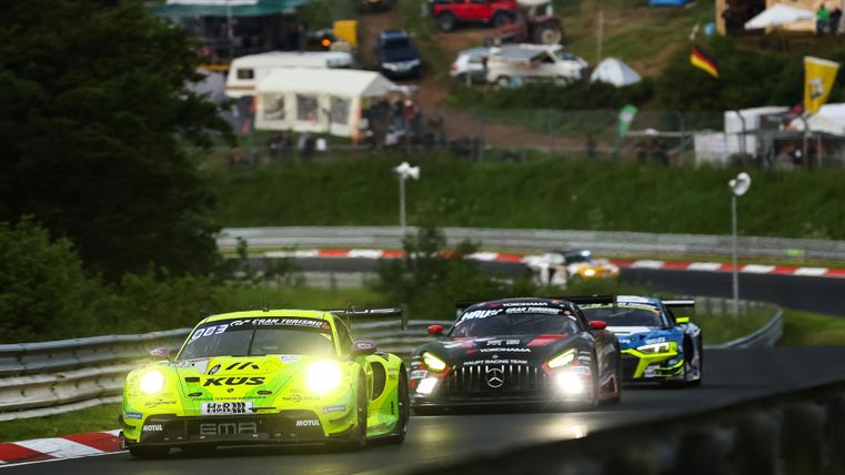 Ein spannendes Autorennen auf einer Rennstrecke mit mehreren Fahrzeugen. Im Hintergrund sind Zeltlager und Zuschauer zu sehen.