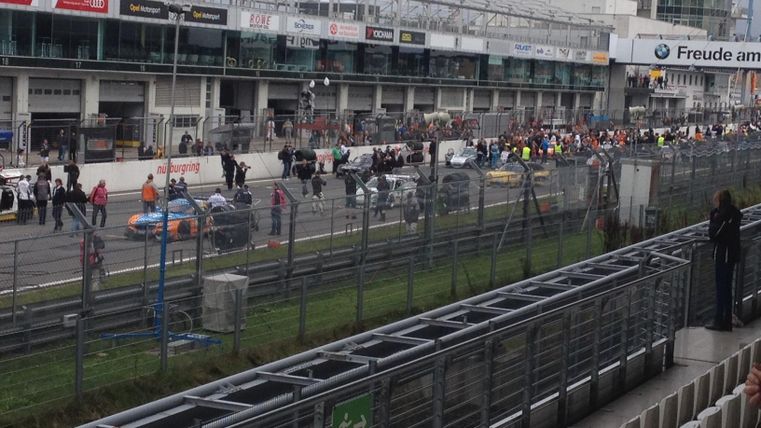 Een racebaan met veel auto's en toeschouwers. De sfeer is levendig, terwijl de voorbereidingen voor de race aan de gang zijn.