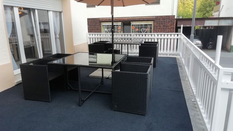 A cozy outdoor area with a table and chairs made of rattan. A parasol provides shade for relaxing hours.