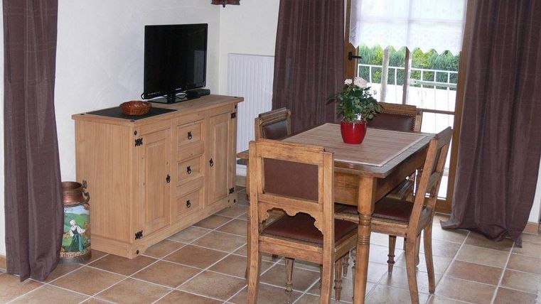Een gezellige woonkamer met een houten tafel en stoelen. Een televisie staat op de commode, en een plantenpot geeft leven aan de ruimte.