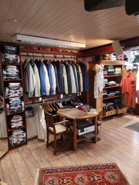 Ein bunter Bekleidungsladen mit einer Vielzahl von Hemden und Jacken an den Wänden. In der Mitte steht ein Tisch mit einem Stuhl.