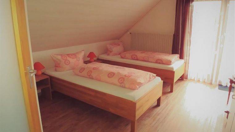 A bright bedroom with two single beds and pink bedding. Large windows let in plenty of daylight.