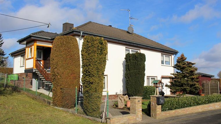 A modern house with a bright facade and a front yard. Well-kept hedges are in the garden, and a staircase leads to the entrance.