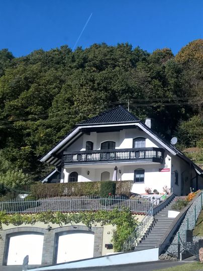 A beautiful house with a balcony, surrounded by trees. In the background, a clear blue sky can be seen.