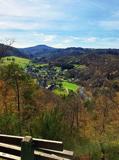 Ein schöner Ausblick auf ein malerisches Dorf in einer grünen Landschaft. Die Umgebung ist von Bäumen und Hügeln umgeben, unter einem klaren blauen Himmel.
