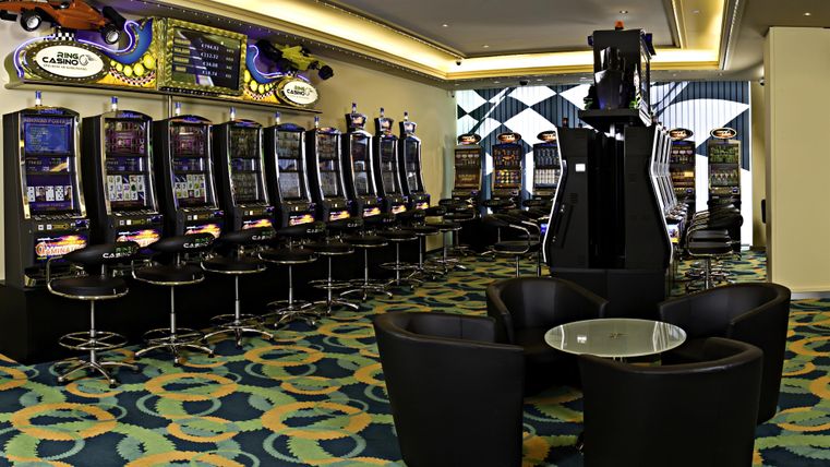 A modern casino with several slot machines. There are comfortable seating areas and a colorful carpet.