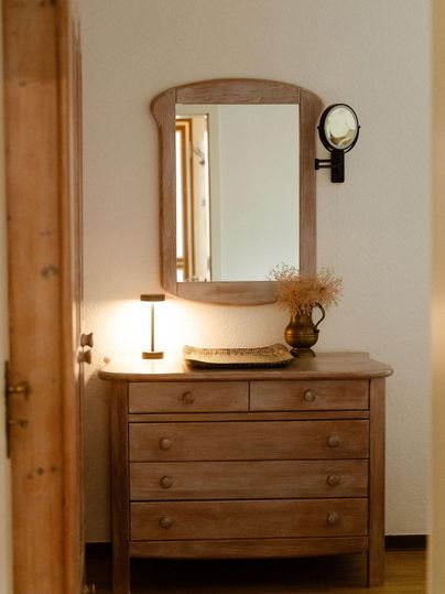 Holzkommode und einem Spiegel im Schlafraum. Ein sanftes Licht beleuchtet den Raum und schafft eine einladende Atmosphäre.