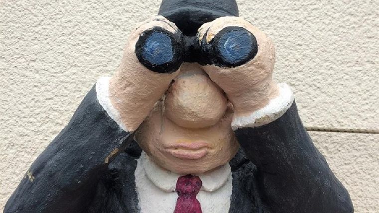 A statue of a man in a suit, looking through binoculars. He has a thoughtful expression and is sitting on a table.