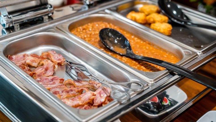 Een buffet met verschillende gerechten. Te zien zijn knapperige spek, bonen en gefrituurde aardappelknödel.