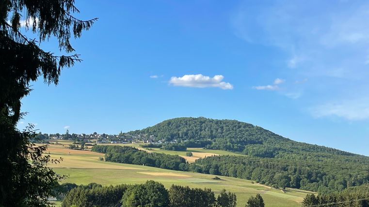 Un paysage verdoyant avec des collines douces sous un ciel bleu. À l'arrière-plan, on voit un village et des prairies.