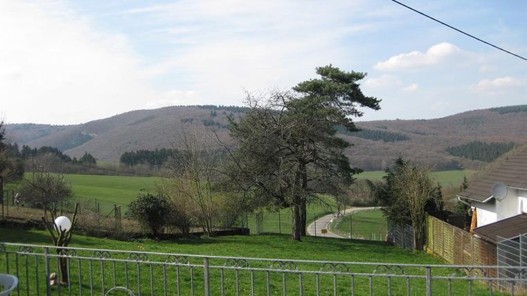 Eine grünen Landschaft mit sanften Hügeln im Hintergrund. Im Vordergrund befindet sich ein gepflegter Garten mit einem Zaun.