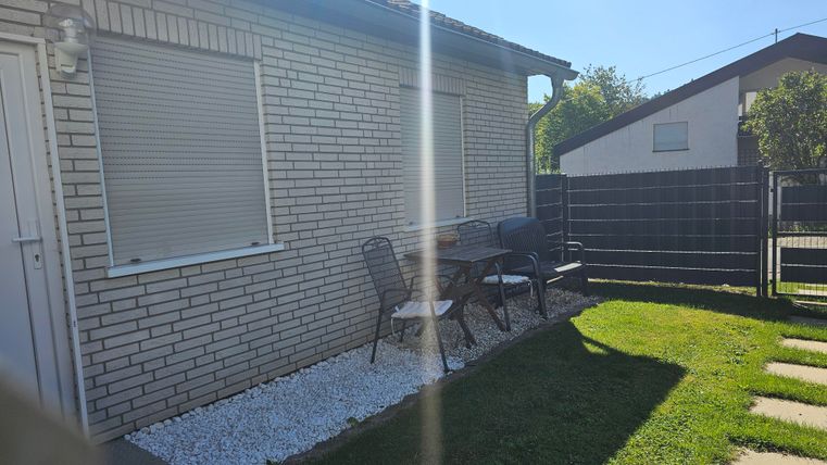 A modern house with a small terrace and two chairs. The garden is neatly designed with grass and gravel.